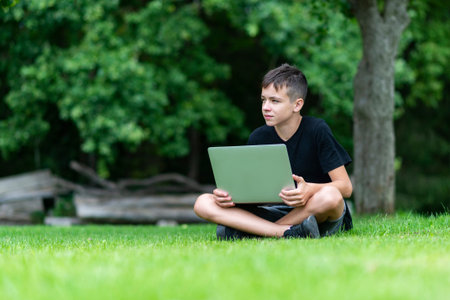 Boy sitting on the grass studying with laptop in the park, Outdoor learning conceptの写真素材