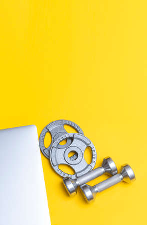 Grey dumbbells and laptop for fitness training on yellow background. Workout online home. Vertical sport poster, greeting cards, headers, website.の写真素材