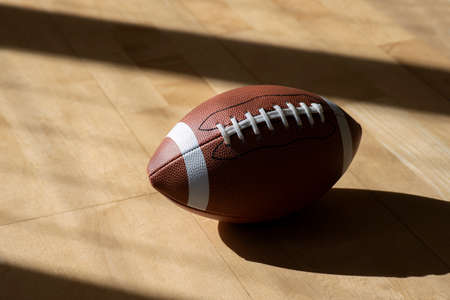 American football ball on hardwood court floor with natural lighting. Workout online concept. Horizontal sport poster, greeting cards, headers, website.の写真素材