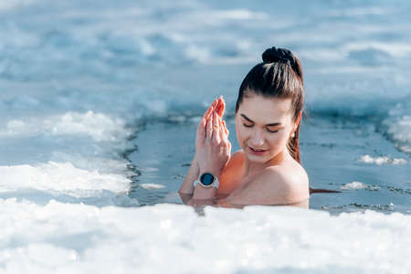 Girl with bikini and a watch in frozen lake ice hole. Woman hardening the body in cold water. Good immunity is protection against many diseases. Vintage color filterの写真素材