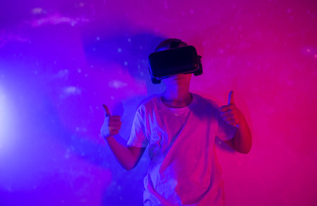 Young boy playing VR goggle on neon lighting. People, technology and cyberspace concept