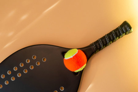 Black professional beach tennis racket and ball on beige background. Horizontal sport theme poster,...