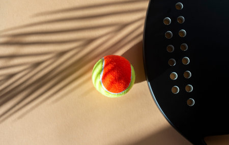 Black professional beach tennis racket and ball on beige background. Horizontal sport theme poster,...