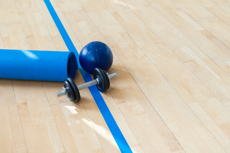 Blue color dumbbells, medicine ball and gym mat on wooden surface. Concept of rehabilitation and...