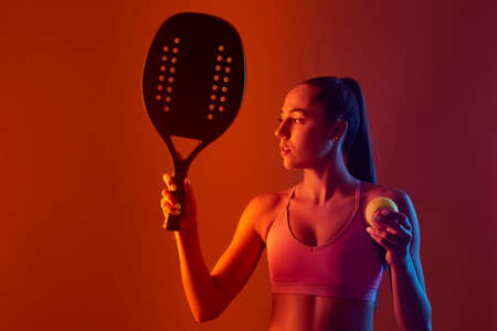 Young girl playing beach tennis on red color background . Professional sport concept. Horizontal sport theme poster, greeting cards, headers, website and appの写真素材