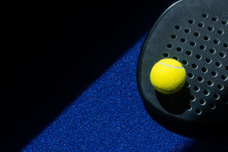 Black professional paddle tennis racket and ball with natural lighting on blue background. Horizontal sport theme poster, greeting cards, headers, website and appの写真素材