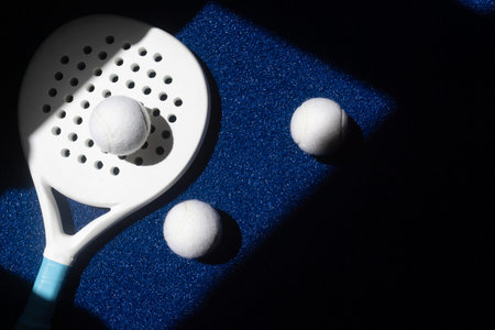 White professional paddle tennis racket and white balls with natural lighting on blue background....