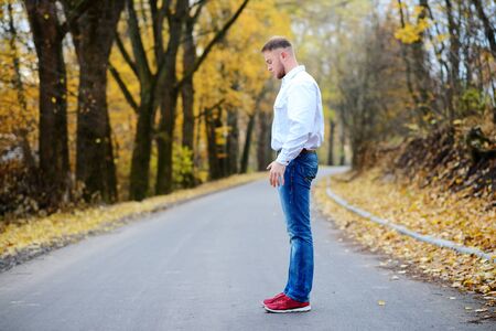 one guy sitting in profile on autumn roadの写真素材