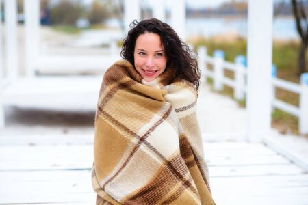 beautiful girl dressed in a blanket on the beach in gorgeous autumn dayの写真素材