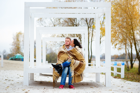 Young couple embracing and covered with a warm blanket sitting on autumn beachの写真素材