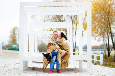 Young couple embracing and covered with a warm blanket sitting on autumn beachの写真素材