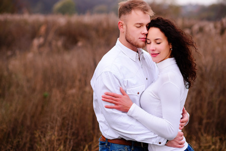 young couple embrace in autumnal landscapes with closed eyes, white dressの写真素材
