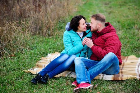 young couple sitting on the plaid and drink coffee from a thermosの写真素材