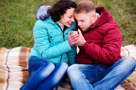 young couple sitting on the plaid and drink coffee from a thermosの写真素材