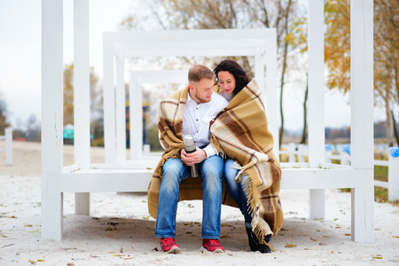 Young couple embracing and covered with a warm blanket sitting on autumn beachの写真素材