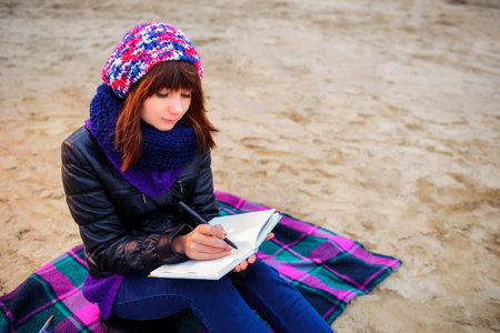 beautiful girl sitting on the beach and has records in a notebookの写真素材