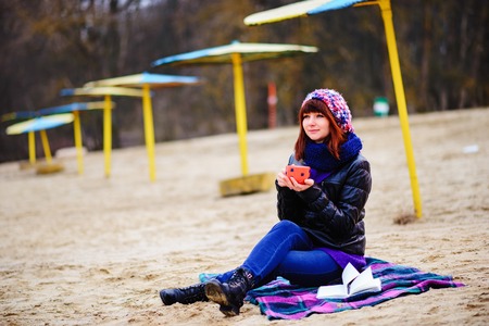 woman drinking coffee from her thermos, enjoying autumn evening by the seaの写真素材