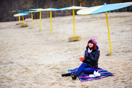 woman drinking coffee from her thermos, enjoying autumn evening by the seaの写真素材