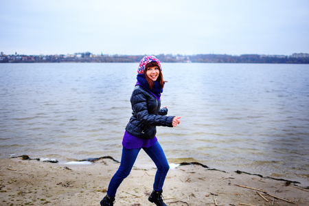 Lifestyle portrait of young Caucasian slim woman with messy long hair wearing black jeans and red shirt walking on windy day outdoor on beach shore at sunset, motion action blurの写真素材