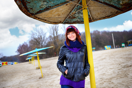 Beautiful girl standing under an umbrella on the beach in autumnの写真素材
