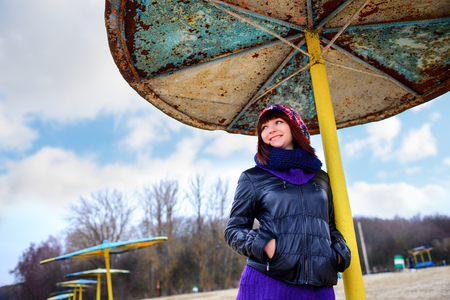 Beautiful girl standing under an umbrella on the beach in autumnの写真素材