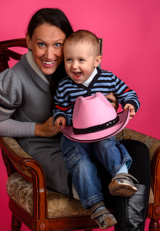 boy sits on a chair next to her mother and holds a cowboy hat, Studioの写真素材