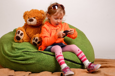 little girl sits on a high green pillow and plays with mobile phoneの写真素材