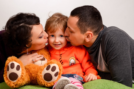 parents kiss little daughter on a white background, Studioの写真素材