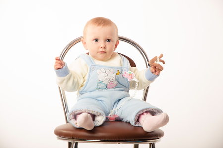 A child sits on a chair, the girl dressed in overallsの写真素材