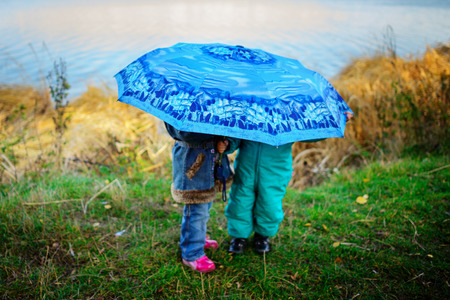 Little girl and boy with umbrella playing in the rain. Kids play outdoor by rainy weather in fall. Autumn fun for children. Toddler kid in raincoat and boots walk in the garden. Summer showerの写真素材