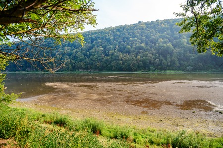 A pile of stones on the bank of the Buller River, with the river in the background and the surrounding high cliffs covered in bush, and the sun setting below a ridge in the background.の写真素材