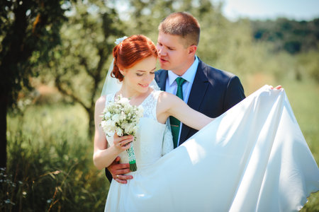 Bride and groom hold each other hands while they walk along the path in parkの写真素材