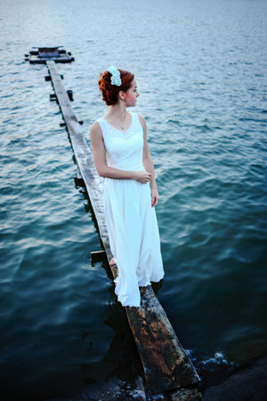 Bride standing on the dock near the water in a white dress.の写真素材