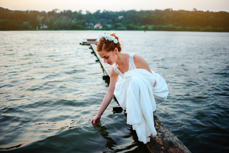 Bride standing on the dock near the water in a white dress.の写真素材