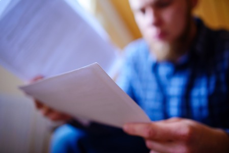Young handsome man sitting on the couch and watches a working paper.の写真素材
