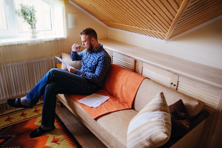 Young handsome man sitting on the couch and watches a working paper.の写真素材