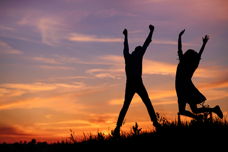 A young man with his girlfriend jump on background sunset silhouette.の写真素材