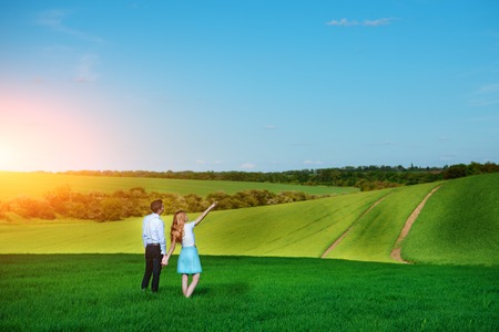 A young couple standing in the field, the girl shows her hand to the sky.の写真素材