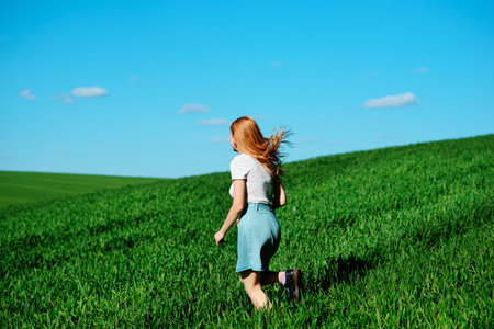 Young beautiful woman running on a green field.の写真素材