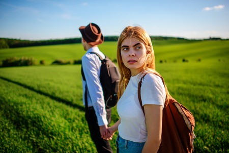 A pair of lovers are holdings their hands together on a green field. Attractive man and a beautiful woman are walking between meadow.の写真素材