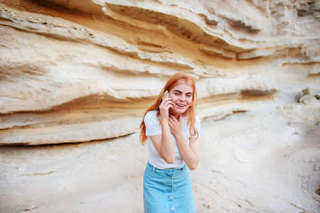 A beautiful woman is smiling and talking by smartphone on the background of a sand quarry.の写真素材