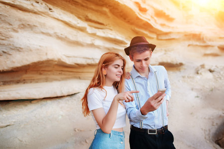 Attractive man and beautiful woman are looking at the screen of a smartphone on the background of a sand quarry.の写真素材