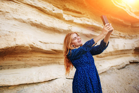 Beautiful woman smiling and looking at the screen of a tablet and making selfie on the background of a sand quarry.の写真素材