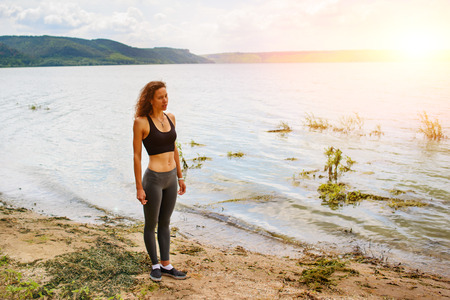 A beautiful sporty woman standing on the shore of a lake in sportswear and preparing for an exercising.の写真素材