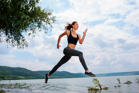 A beautiful sporty woman runing on the shore of a lake in sportswear. Girl is exercising.の写真素材