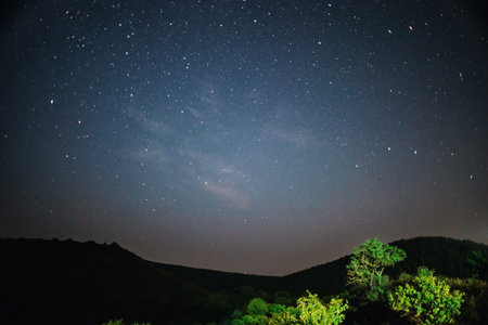 A clear night sky with a hill and trees in the foreground.の写真素材