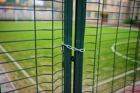 Close up metallic net-shaped green fence that closed and wrapped by chain on a background of school football field.の写真素材