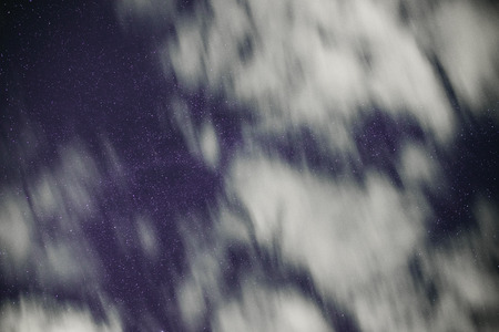 Background of dark-blue night sky with countless twinkle stars and moving white clouds upon on it.の写真素材