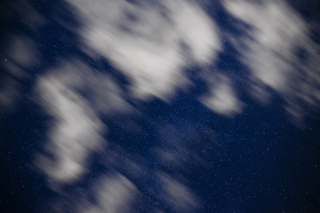 Background of dark-blue night sky with countless twinkle stars and moving white clouds upon on it.の写真素材