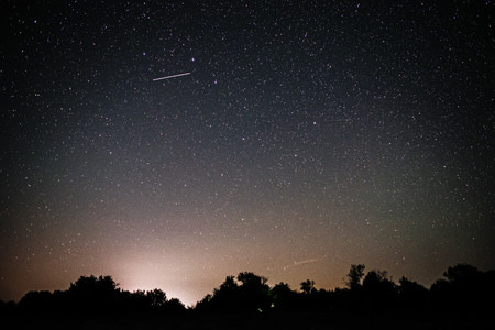 Background of bright starry night sky with lights upon on it and silhouette of trees.の写真素材